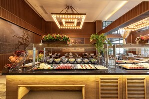 A buffet with various food items, a statue, and a chandelier. - By The Marina Hotel (Mersin)