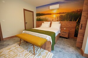 Un dormitorio con cama, un banco, cabecero de madera, mesita de noche y un mural en la pared de un atardecer sobre el agua.