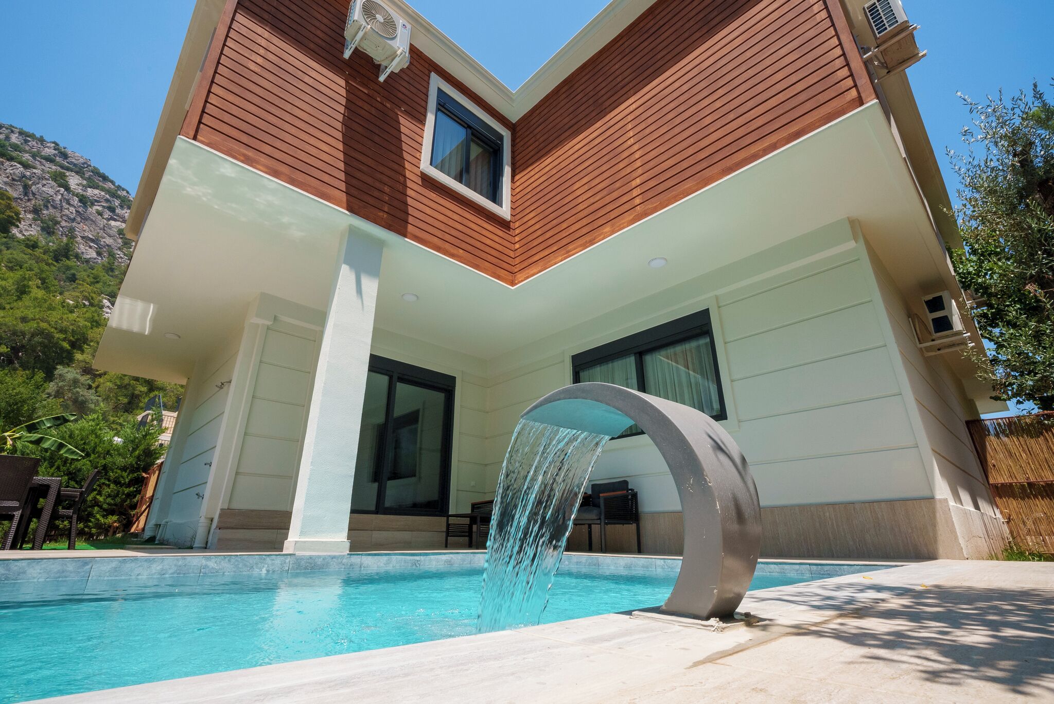 A modern building with a swimming pool, a waterfall feature, and a view of a mountainous landscape.