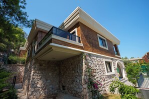Una casa de dos pisos con base de piedra, un balcón y un pequeño jardín.