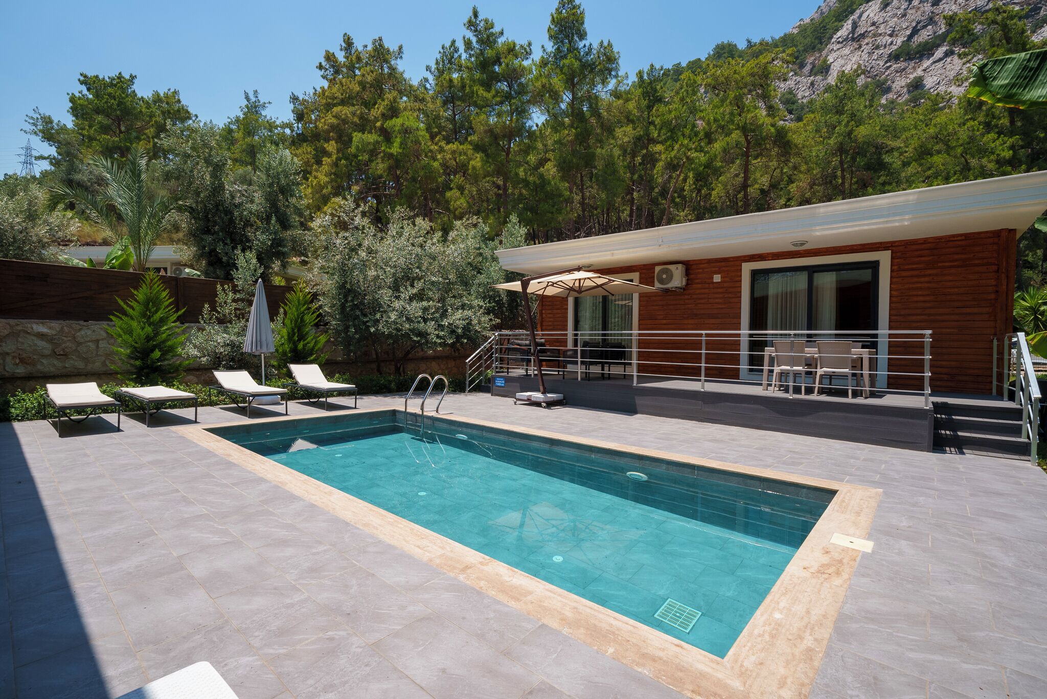 A swimming pool with lounge chairs, a wooden building with a balcony, and a mountainous backdrop.