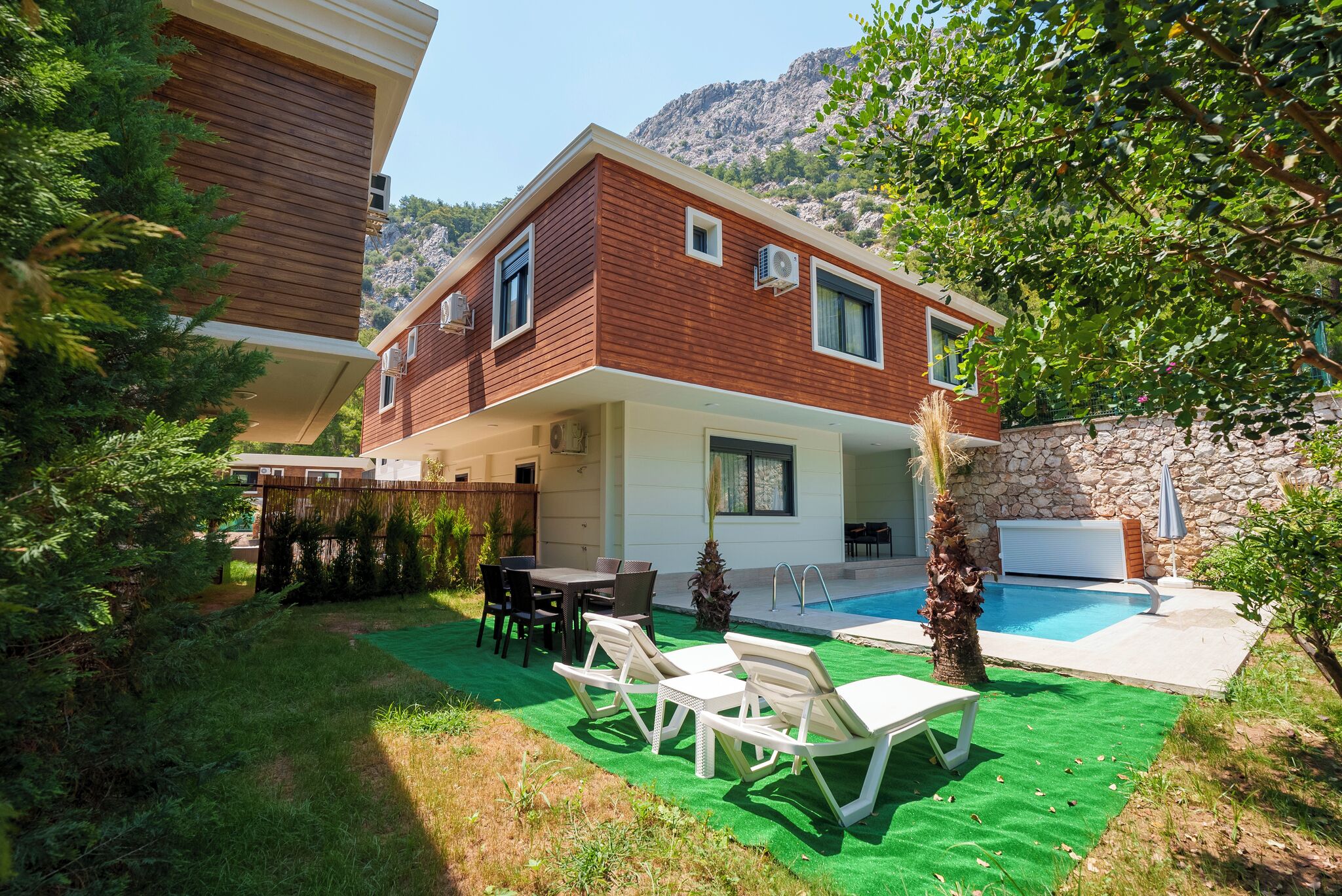 A two-story house with a swimming pool, outdoor furniture, and a stone wall.