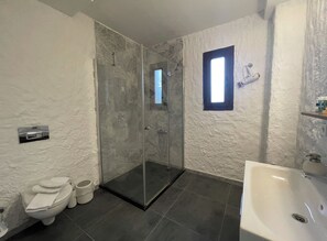 Ein Badezimmer mit einer Duschkabine, Toilette, Waschbecken und einem kleinen Fenster.