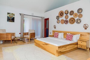 A bedroom with a wooden bed, two wicker chairs, a small table, and a wall decorated with various woven plates. - Shose Farmhouse & Chalets (Moshi)