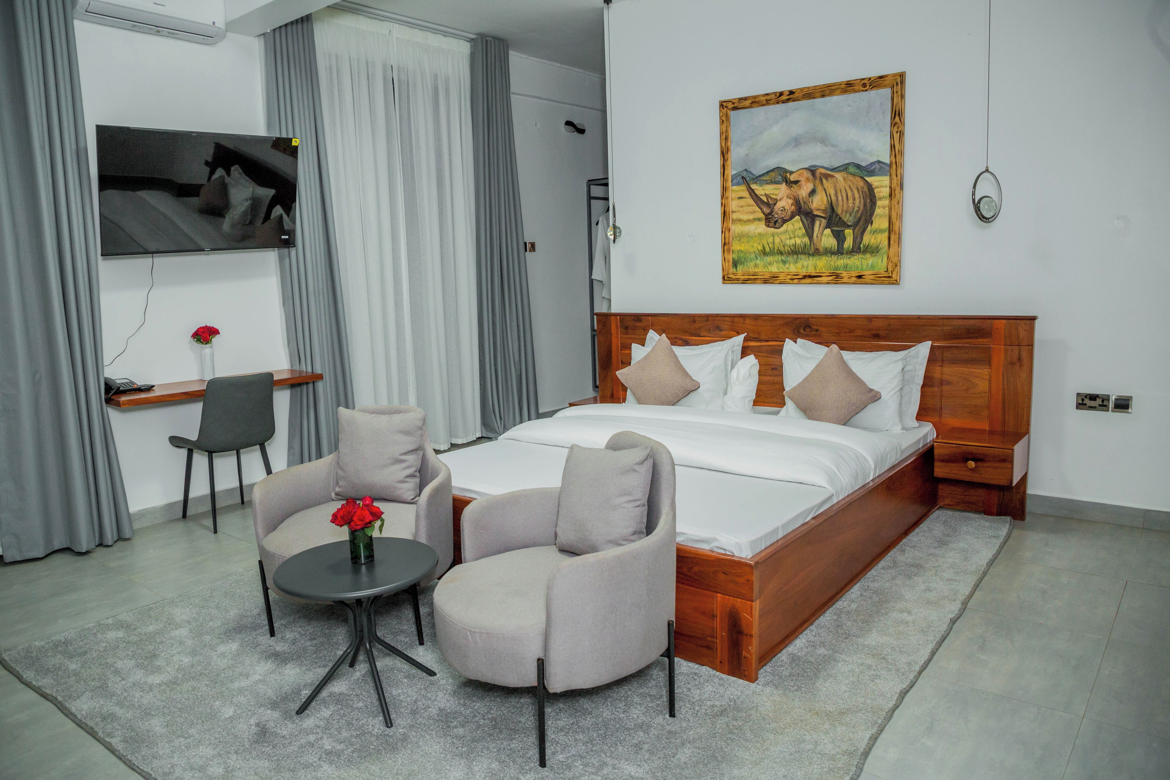 Habitació d'hotel amb un llit gran, dos seients, una taula petita amb un vas, un televisor i un quadre d'un rinoceront.