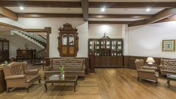 A spacious living room with a grand staircase, wooden furniture, and a chandelier.