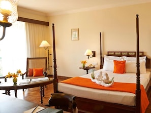 Una cama con dosel, con un edredón naranja, una mesita de noche con una lámpara y una silla con cojín.