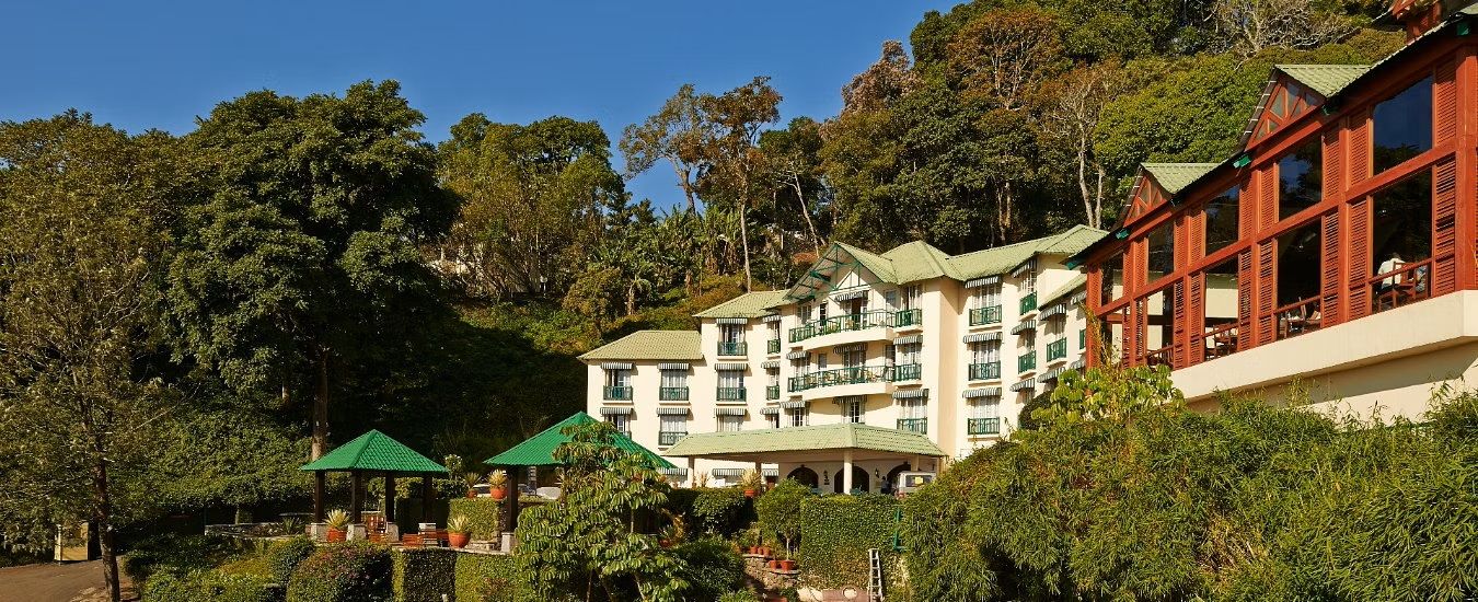 A multi-story hotel with balconies, surrounded by lush greenery and trees.