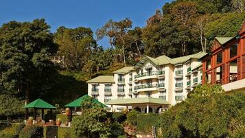 A multi-story hotel with balconies, surrounded by lush greenery and trees.