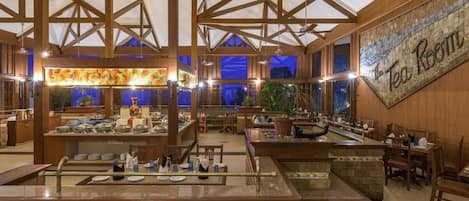 Un restaurante espacioso con techos altos y vigas de madera, que cuenta con una zona de bar central y varias mesas de comedor.