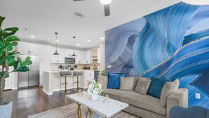 Ein modernes Wohnzimmer mit einem Marmor-Couchtisch, einem Sofa mit blauen Kissen und einem großen abstrakten Gemälde an der Wand.