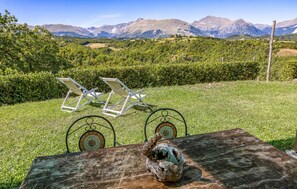 Ein Tisch mit einem rustikalen Topf und zwei Liegestühlen auf einer Wiese mit Blick auf die Berge.