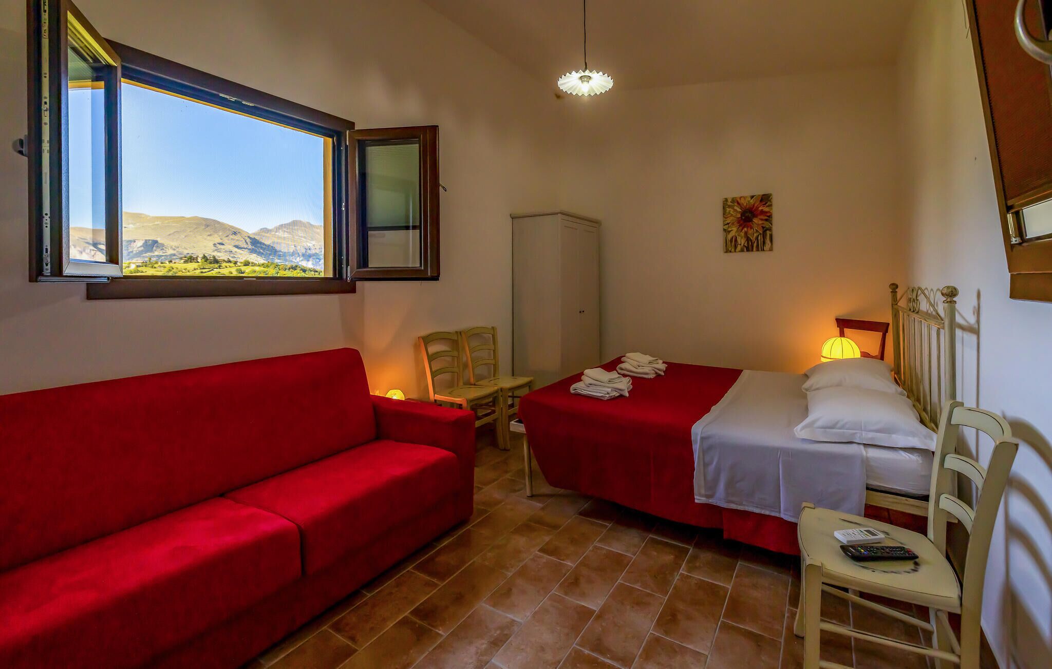 A room with a red sofa, two single beds, a small table, a chair, a wardrobe, and a window with a mountain view.