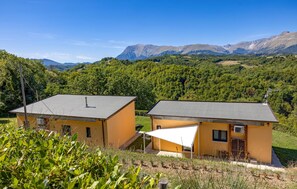 Zwei gelbe Gebäude mit flachen Dächern, umgeben von Grünpflanzen und Bergen im Hintergrund.