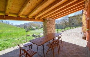 Un espace extérieur aménagé, abrité et doté d’une table et de bancs en pierre, offrant une vue sur un vignoble et un bâtiment en pierre.