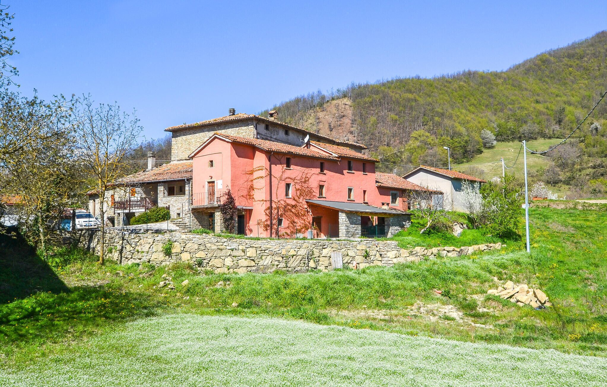 Un bâtiment aux murs de pierre, doté d’une façade rouge, d’un balcon et offrant une vue sur une colline verdoyante.
