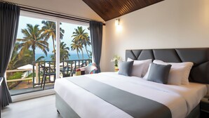 A bedroom with a large bed, a view of palm trees and the ocean, and a balcony with chairs. - Stone Wood Beach Resort- A Party Hotel (Vagator)