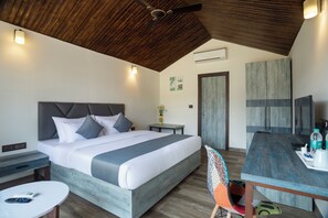 A modern hotel room with a large bed, a dining table, and a ceiling fan.