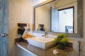 A bathroom with a large mirror, a sink, a hairdryer, and a small potted plant.