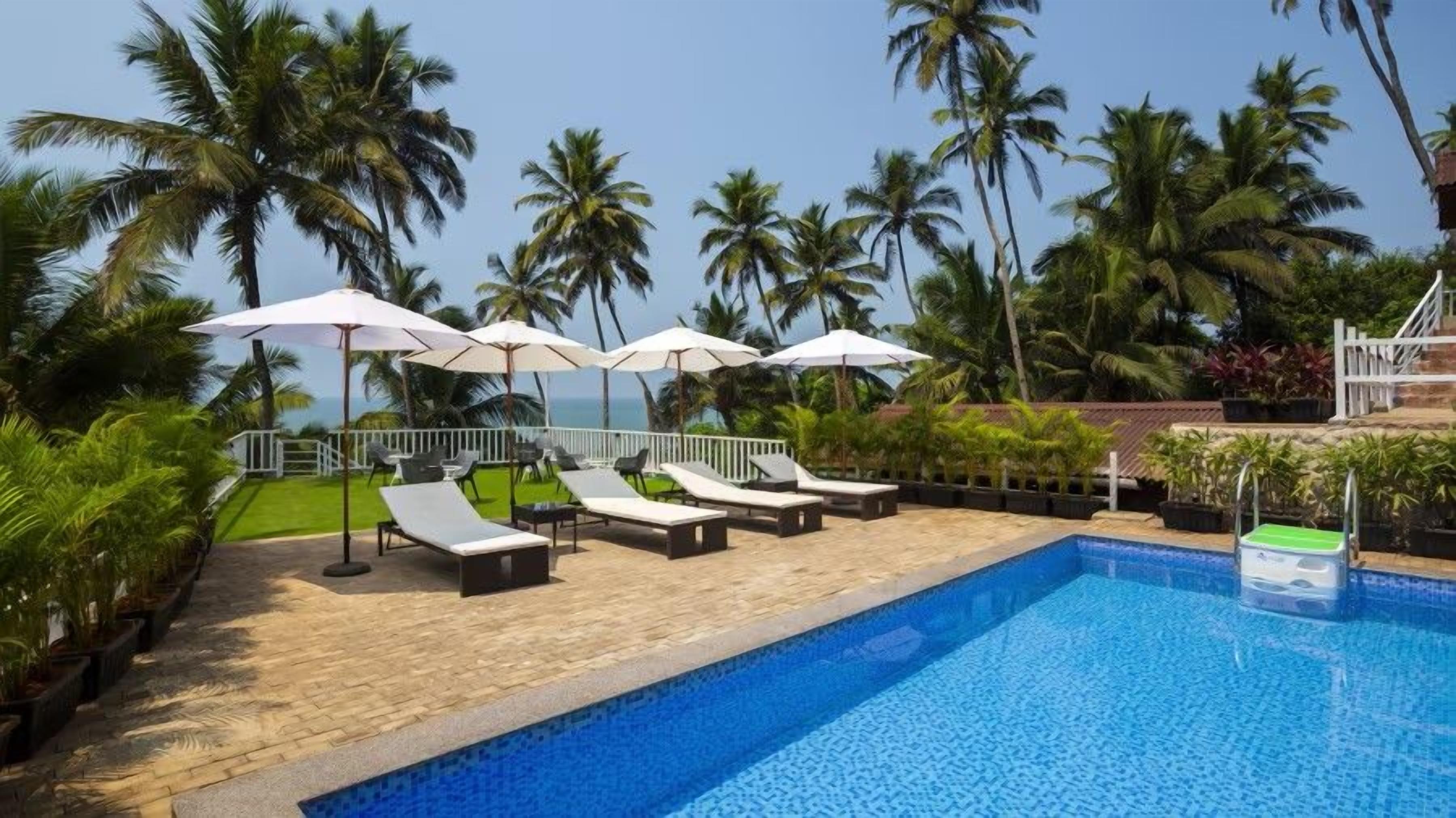 A poolside area with lounge chairs and umbrellas, surrounded by palm trees and a view of the ocean.