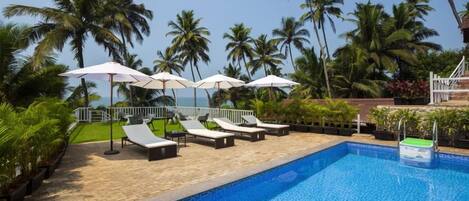 A poolside area with lounge chairs and umbrellas, surrounded by palm trees and a view of the ocean.