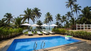 A swimming pool with lounge chairs and umbrellas, surrounded by palm trees. - Stone Wood Beach Resort- A Party Hotel (Vagator)