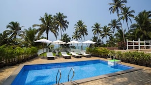 Zwembad met ligbedden en parasols, omringd door palmbomen.
