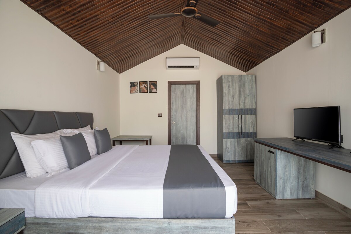 A bedroom with a bed, a TV, and a wooden ceiling.