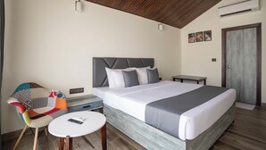 A modern hotel room with a large bed, a colorful chair, a small table, and a wooden ceiling. - Stone Wood Beach Resort- A Party Hotel (Vagator)