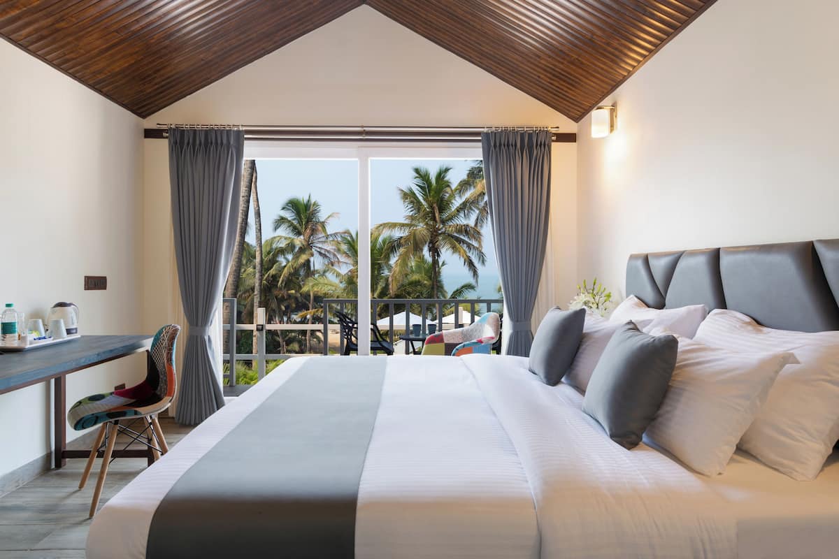 A bedroom with a large bed, a desk, and a view of palm trees.