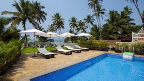 A poolside area with lounge chairs and umbrellas, surrounded by palm trees and a view of the ocean.