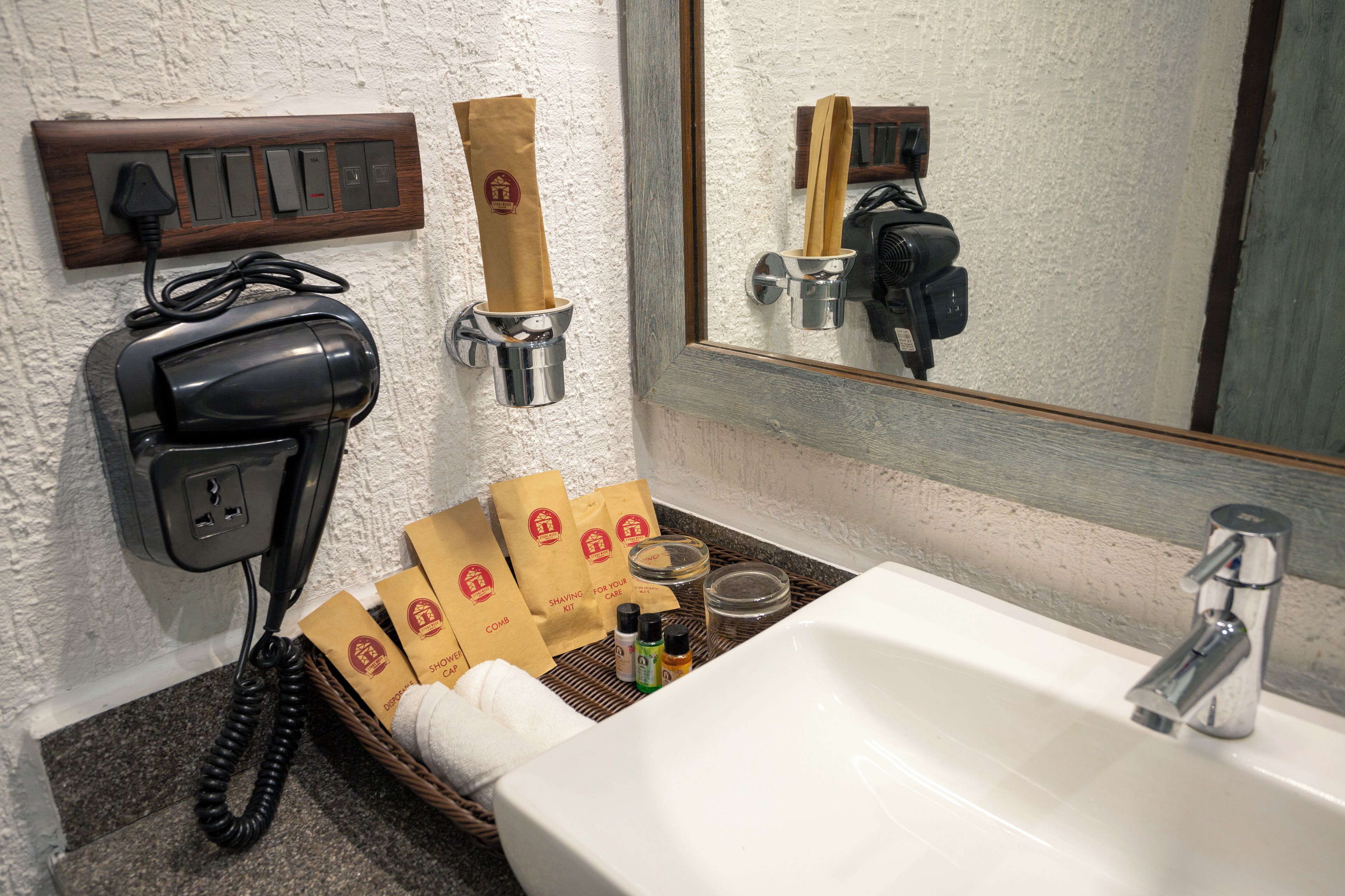 A bathroom with a sink, mirror, hairdryer, and a wall-mounted phone. There are also towels and toiletries in a basket.