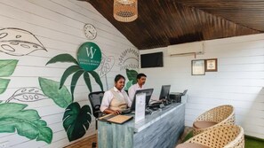A reception desk with a logo, a clock, and a wall mural. - Stone Wood Beach Resort- A Party Hotel (Vagator)