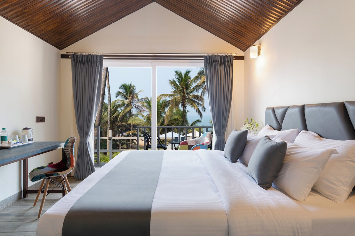 A bedroom with a large bed, a desk, and a view of palm trees.