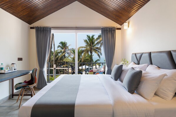 A bedroom with a large bed, a desk, and a view of palm trees.