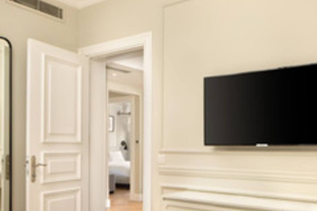 Habitación de hotel con cama, televisión montada en la pared y puerta que da a otra habitación.