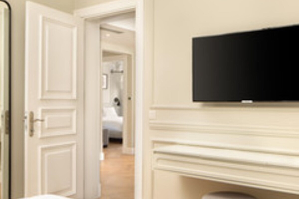 A hotel room with a bed, a television mounted on the wall, and a door leading to another room.