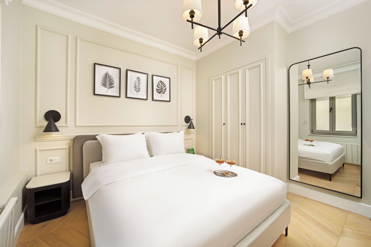 A neatly arranged hotel room with a large bed, bedside tables, a mirror, and framed leaf artwork on the wall.