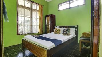 A room with a bed, a wooden wardrobe, a window with curtains, and a small stool.