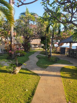 A garden pathway leading to a building with a thatched roof, surrounded by tropical plants and a clear sky. - Tauch Terminal Resort Tulamben & Spa (Rendang)