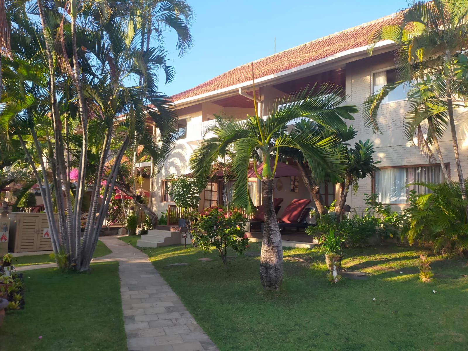 A two-story building with a tiled roof, surrounded by palm trees and a well-maintained lawn.