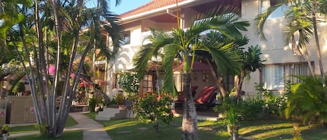 A two-story building with a tiled roof, surrounded by palm trees and a well-maintained lawn.