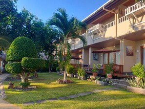 A hotel with a covered outdoor seating area, a well-maintained garden with various plants, and a two-story building with balconies.