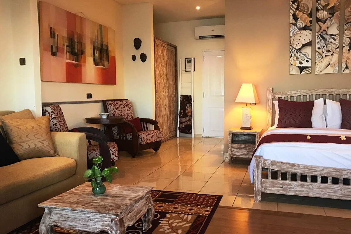 A hotel room with a bed, a sofa, a small table, a lamp, and a decorative wall piece.