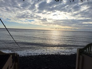 A coastal view with a clear sky and calm sea, a wooden railing, and a rocky shoreline.