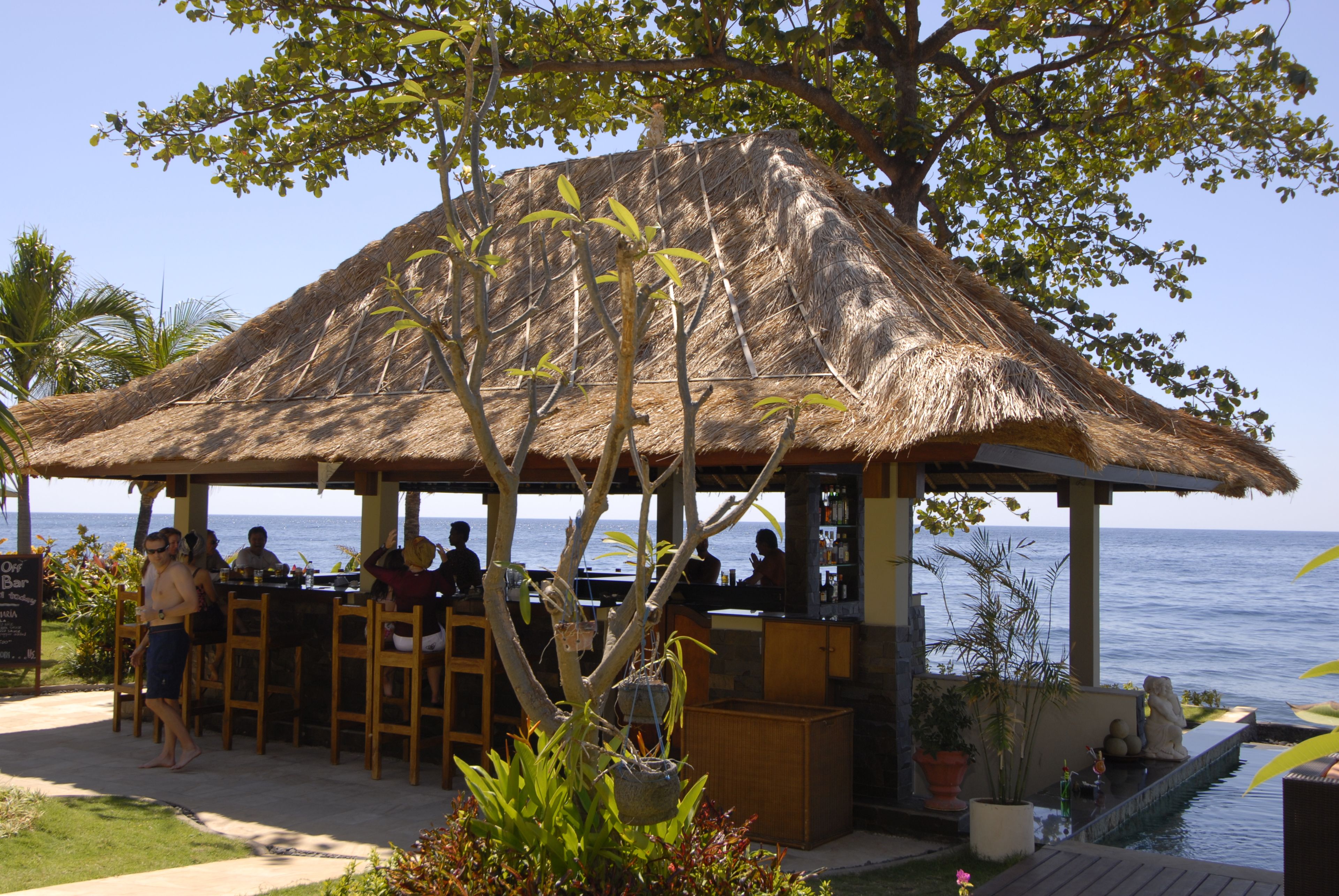 Eine Strohdach-Bar im Freien mit Tischen und Stühlen mit Blick auf das Meer.