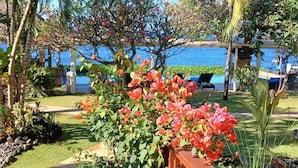 A tropical garden with a wooden deck, palm trees, and a view of the sea.