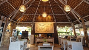 A spacious lobby with a high thatched ceiling, wicker furniture, and a central reception desk.