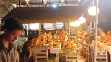 Un comedor con mesas y sillas, una persona sirviendo comida, y diferentes platos y bebidas.