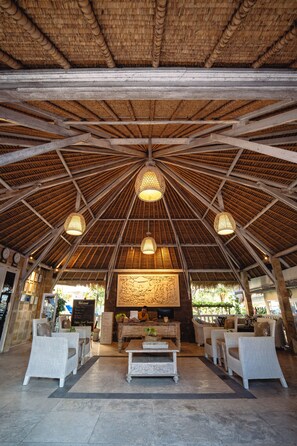 A spacious lobby with a high thatched ceiling, wicker furniture, and a central reception desk.